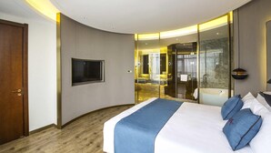 A modern hotel room with a large bed, a television, a bathroom with a bathtub, and a curved wall design. - Mercure Harbin Songbei (Harbin)