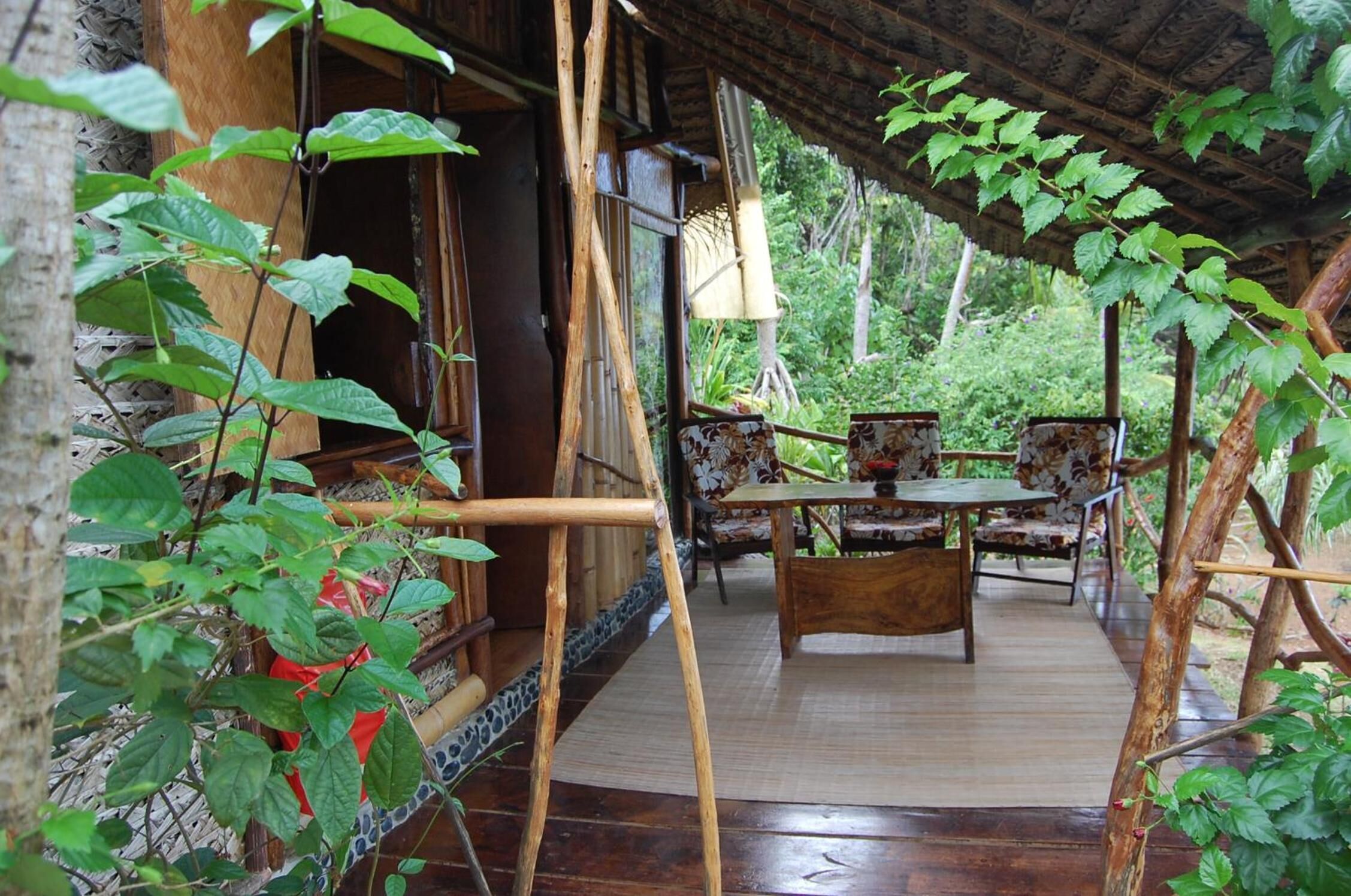 Une terrasse en bois avec une table et des chaises, entourée d’une végétation luxuriante.
