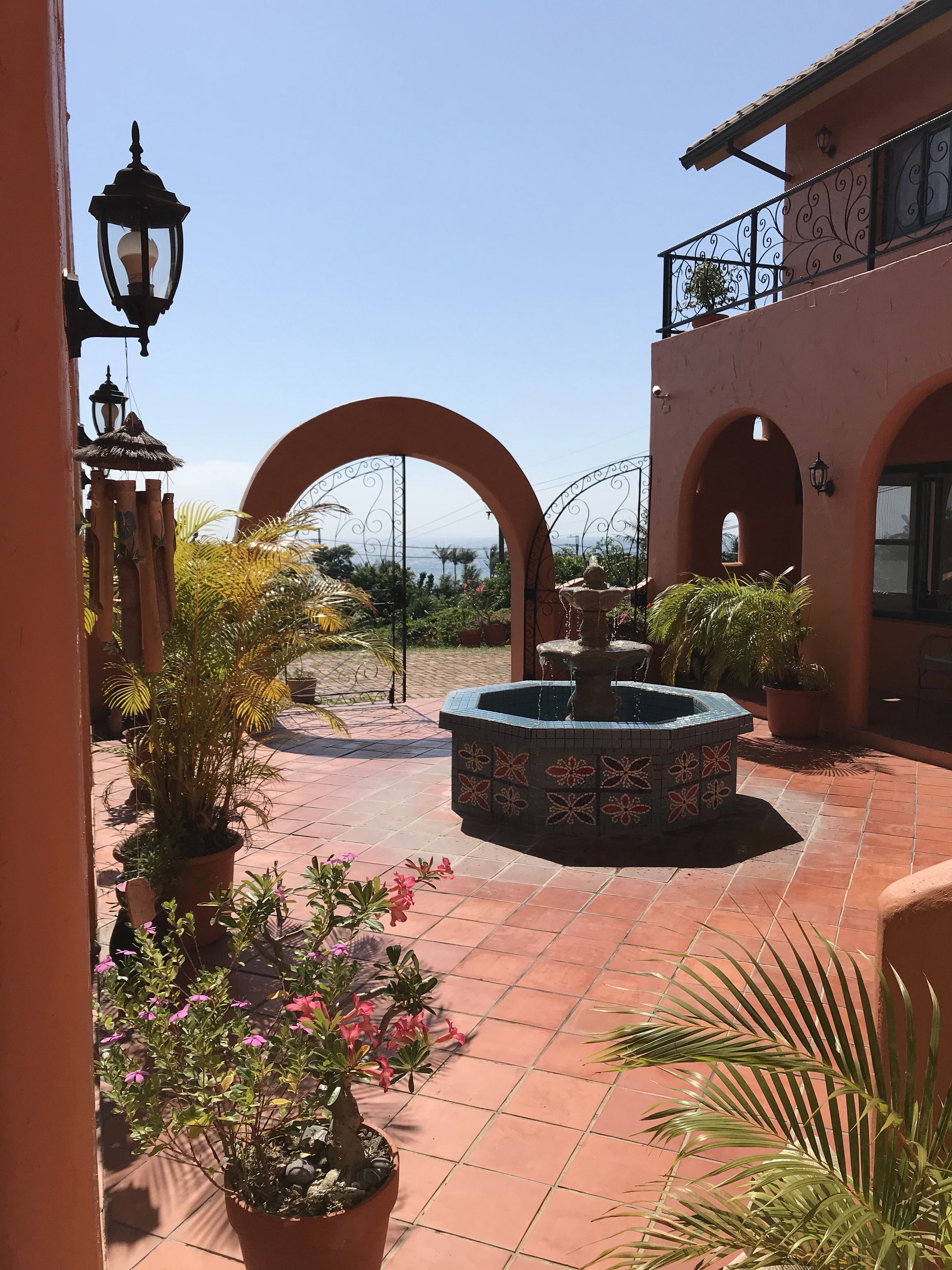 A courtyard with a fountain, potted plants, and a view of the sea.