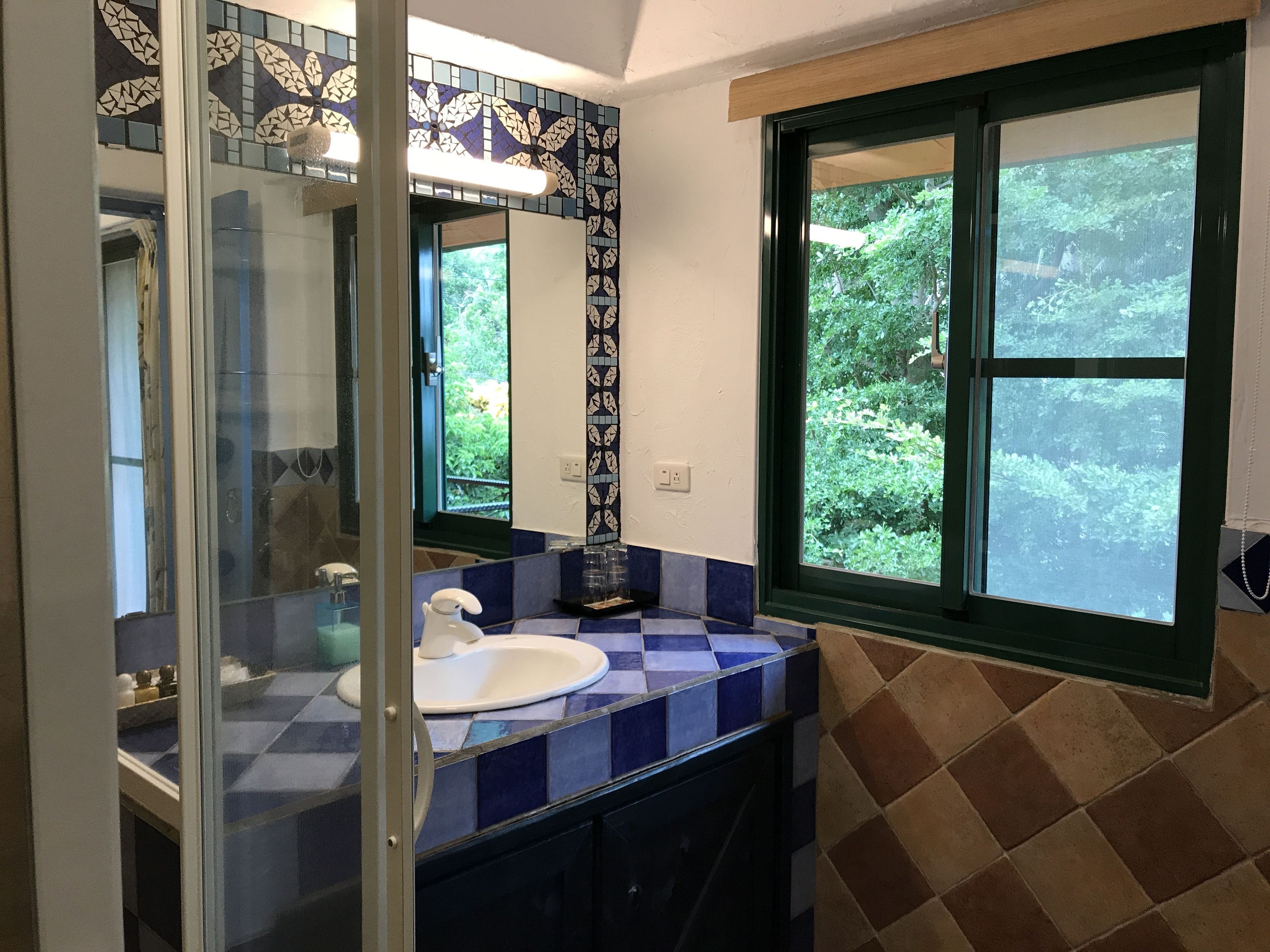 A bathroom with a blue and white checkered tile backsplash, a white sink, and a large window with a view of greenery.