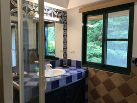 A bathroom with a blue and white checkered tile backsplash, a white sink, and a large window with a view of greenery.