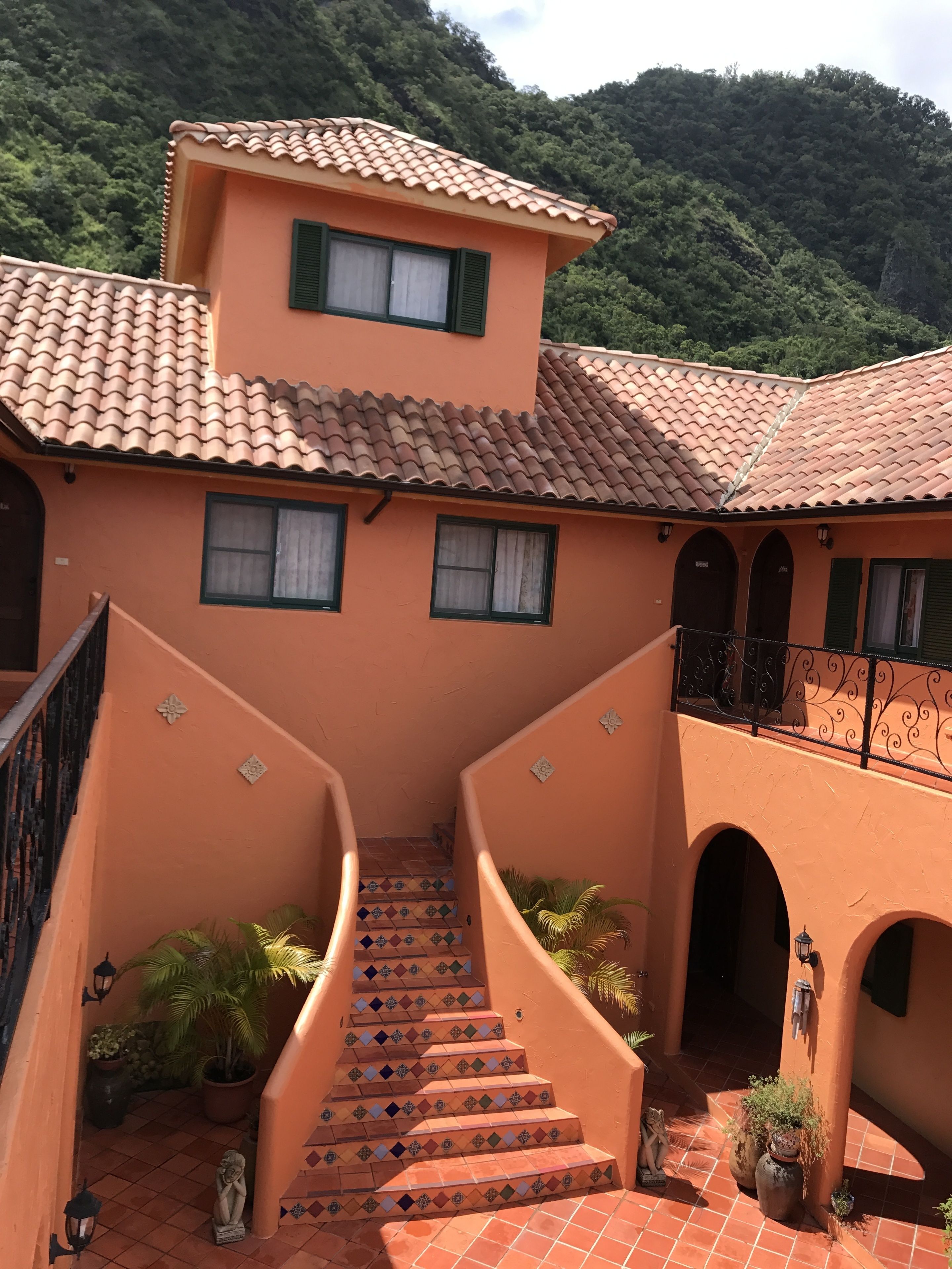 Um edifício com telhado de telhas de terracota, escadaria com ladrilhos estampados e varanda com grades de ferro forjado.