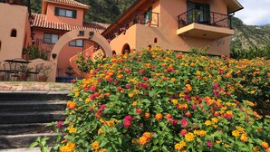 A building with a terracotta roof, a balcony with wrought iron railings, and a lush flower bed in the foreground.