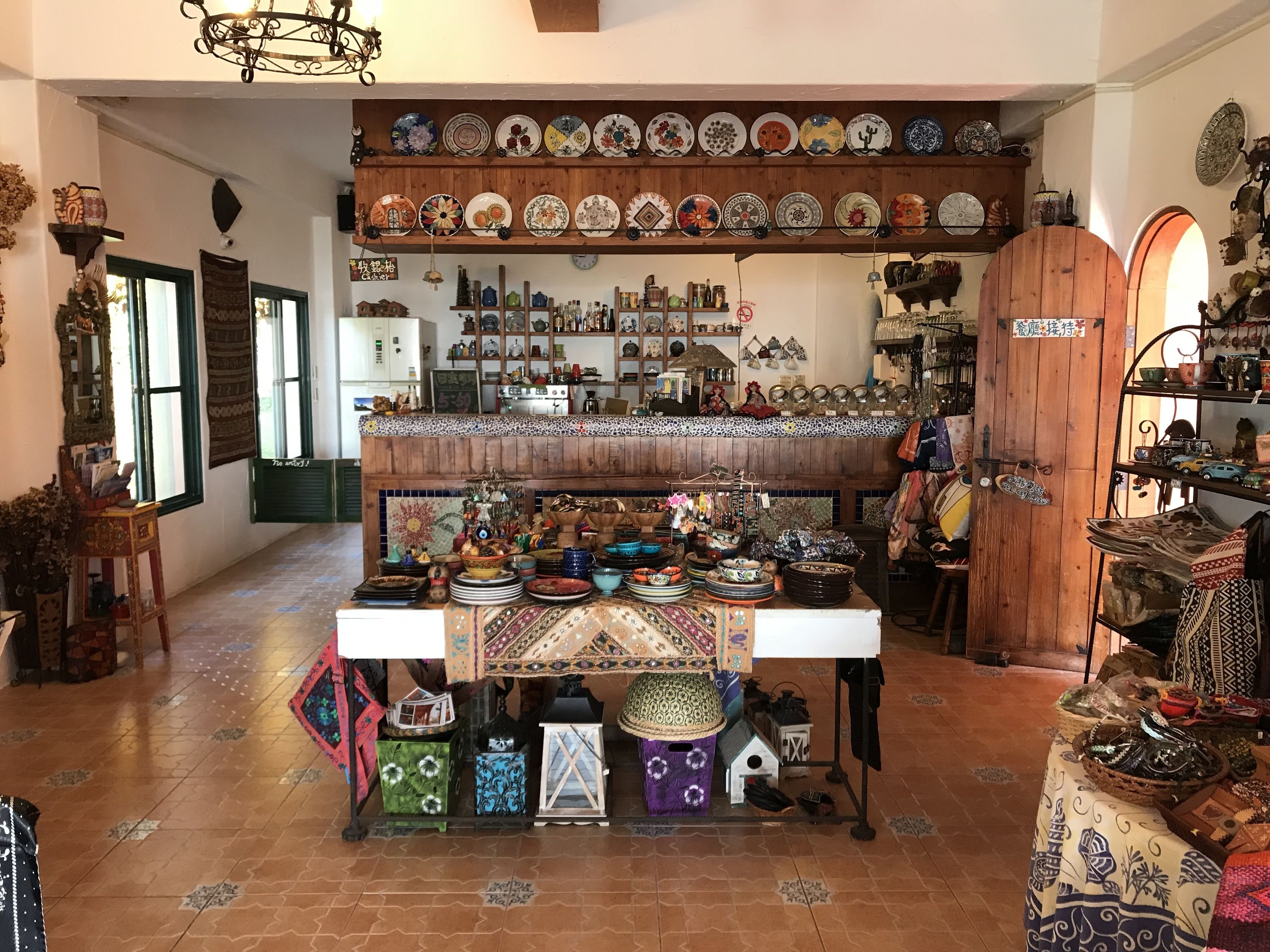 A room with a central table displaying various decorative items and a wall with shelves of plates and ceramics.
