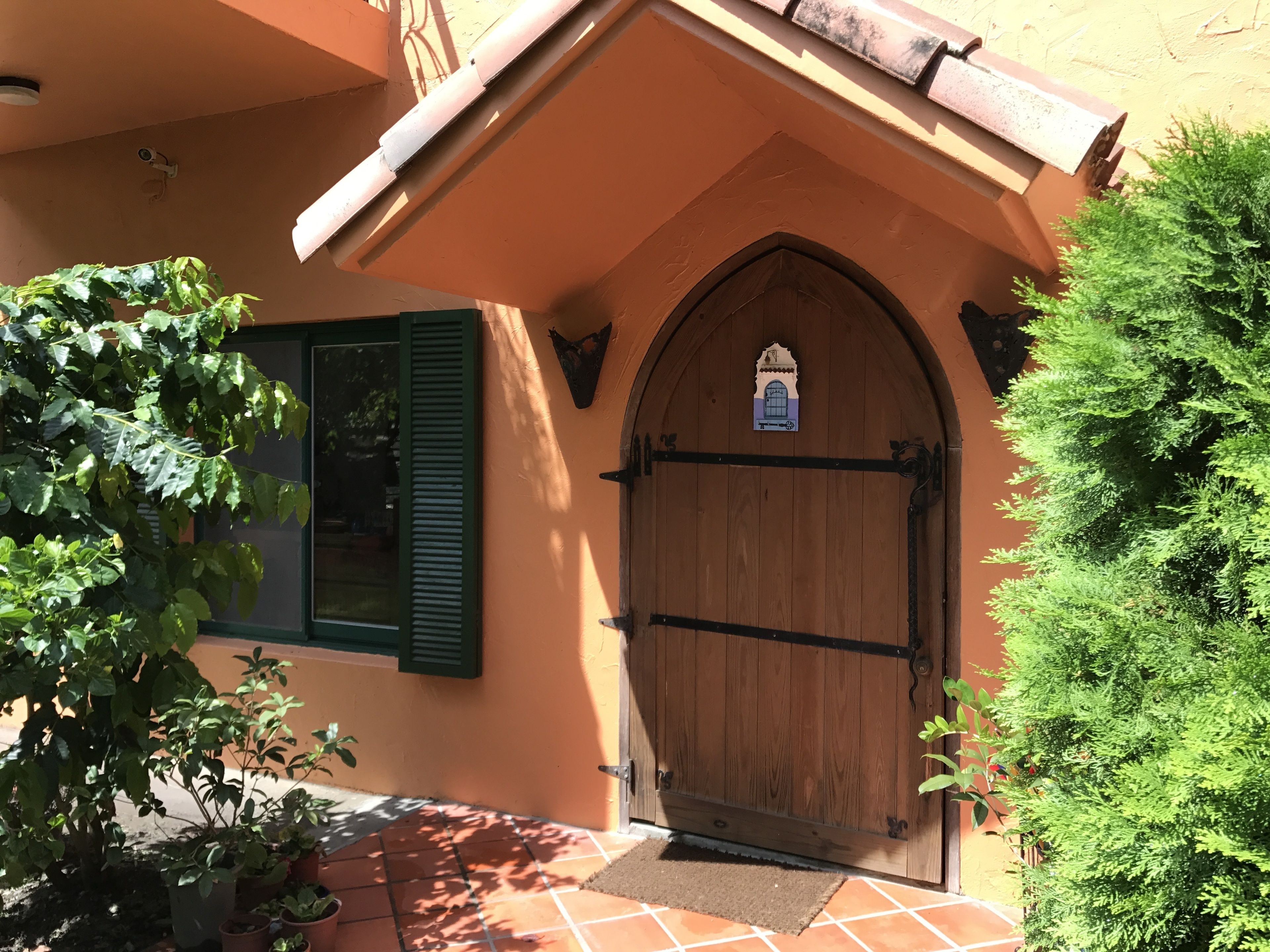 A wooden door with a decorative arch, a green shuttered window, and a small sign above the door.