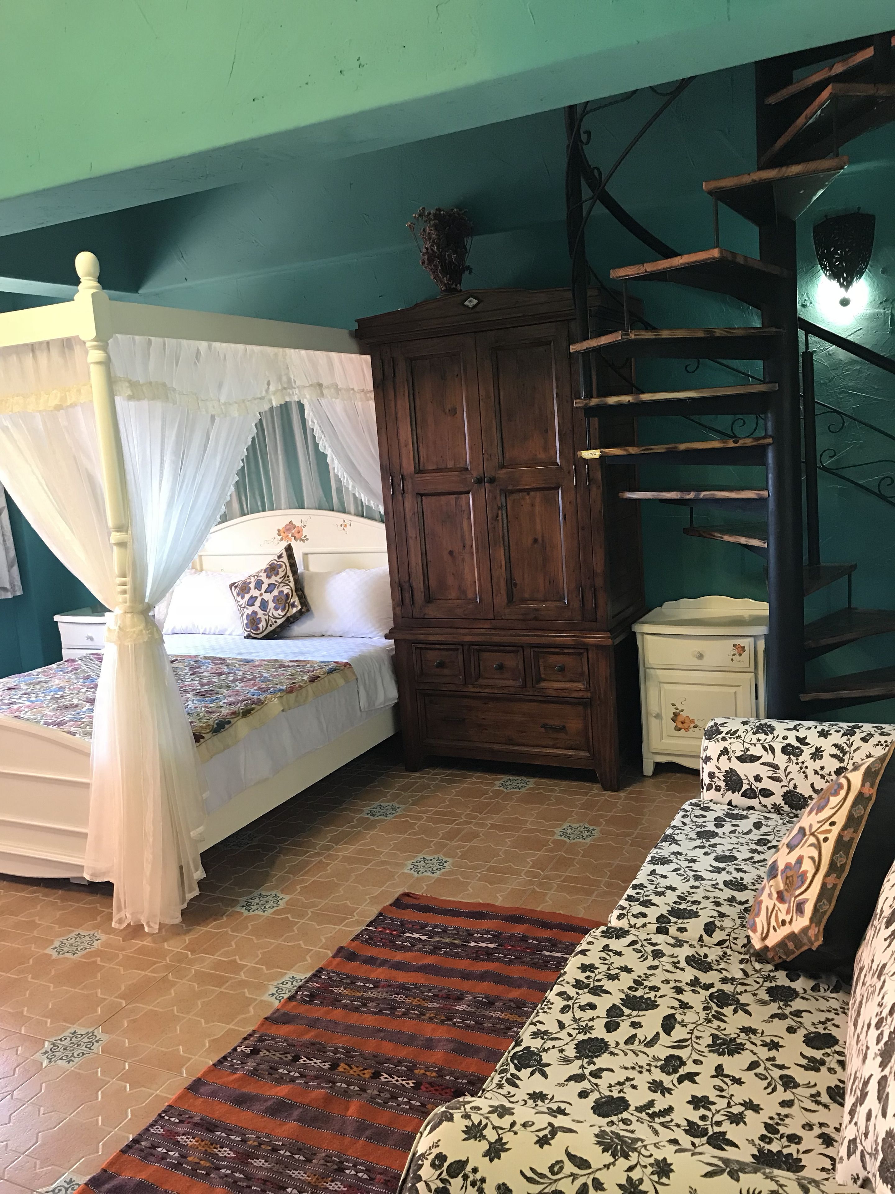 Een slaapkamer met een hemelbed, een houten garderobe, een klein nachtkastje en een gestreept bankje.