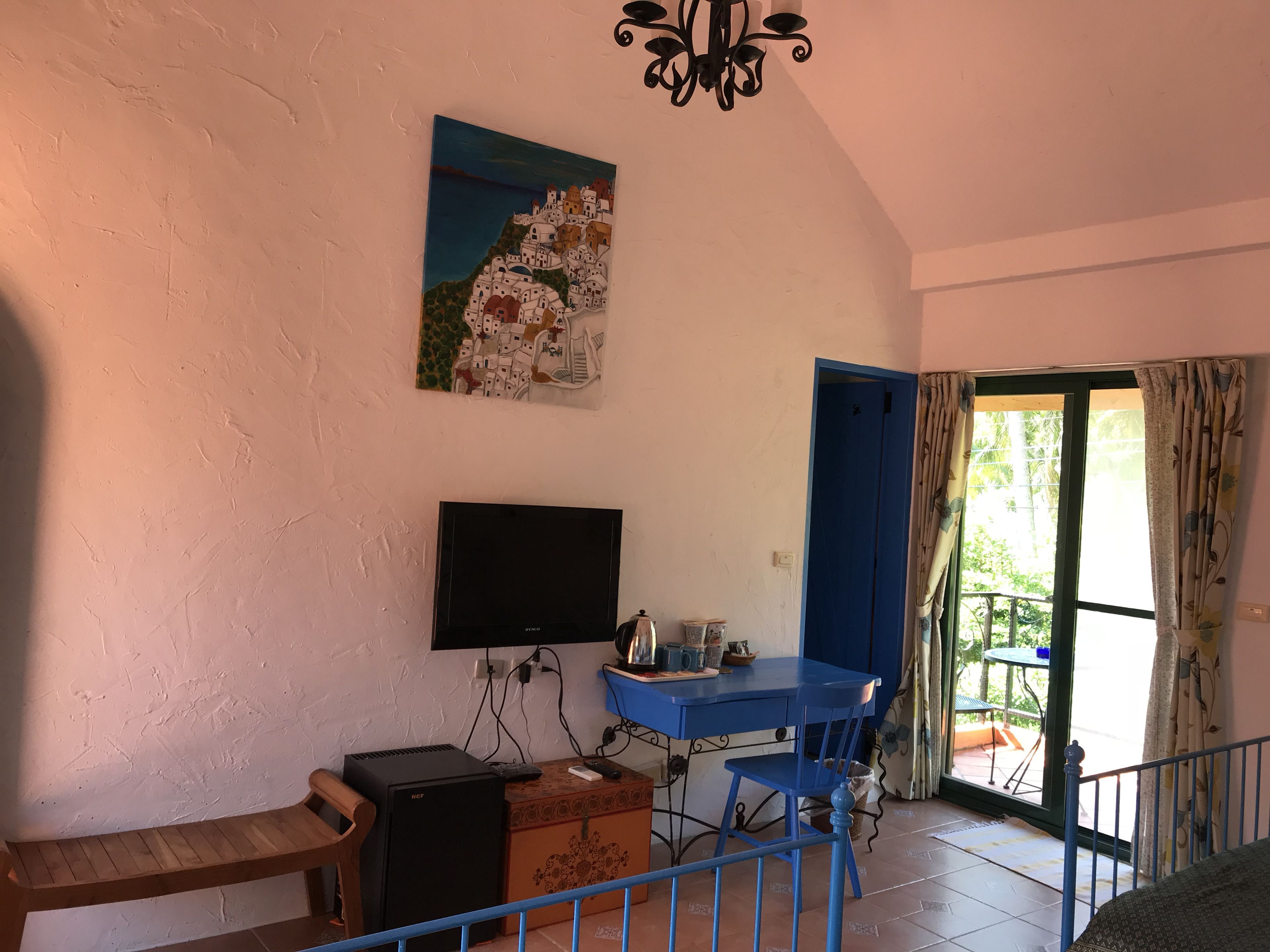 A room with a TV, a desk, a chair, a wooden bench, and a painting on the wall.