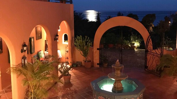 A courtyard with a fountain, potted plants, and a view of the sea at dusk.
