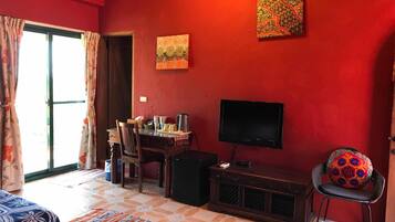 A room with a red wall, a television, a dining table with chairs, and a window with curtains.