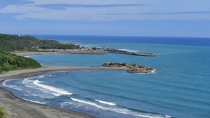 A coastal landscape with a beach, rocky outcrops, and a lighthouse in the distance.