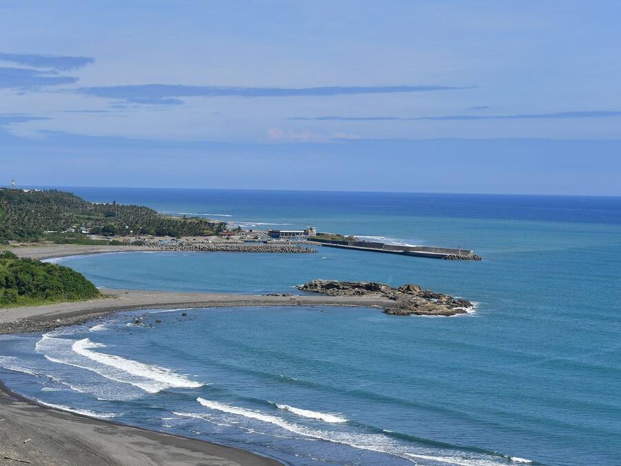 Un paisaje costero con playa, afloramientos rocosos y un faro a lo lejos.
