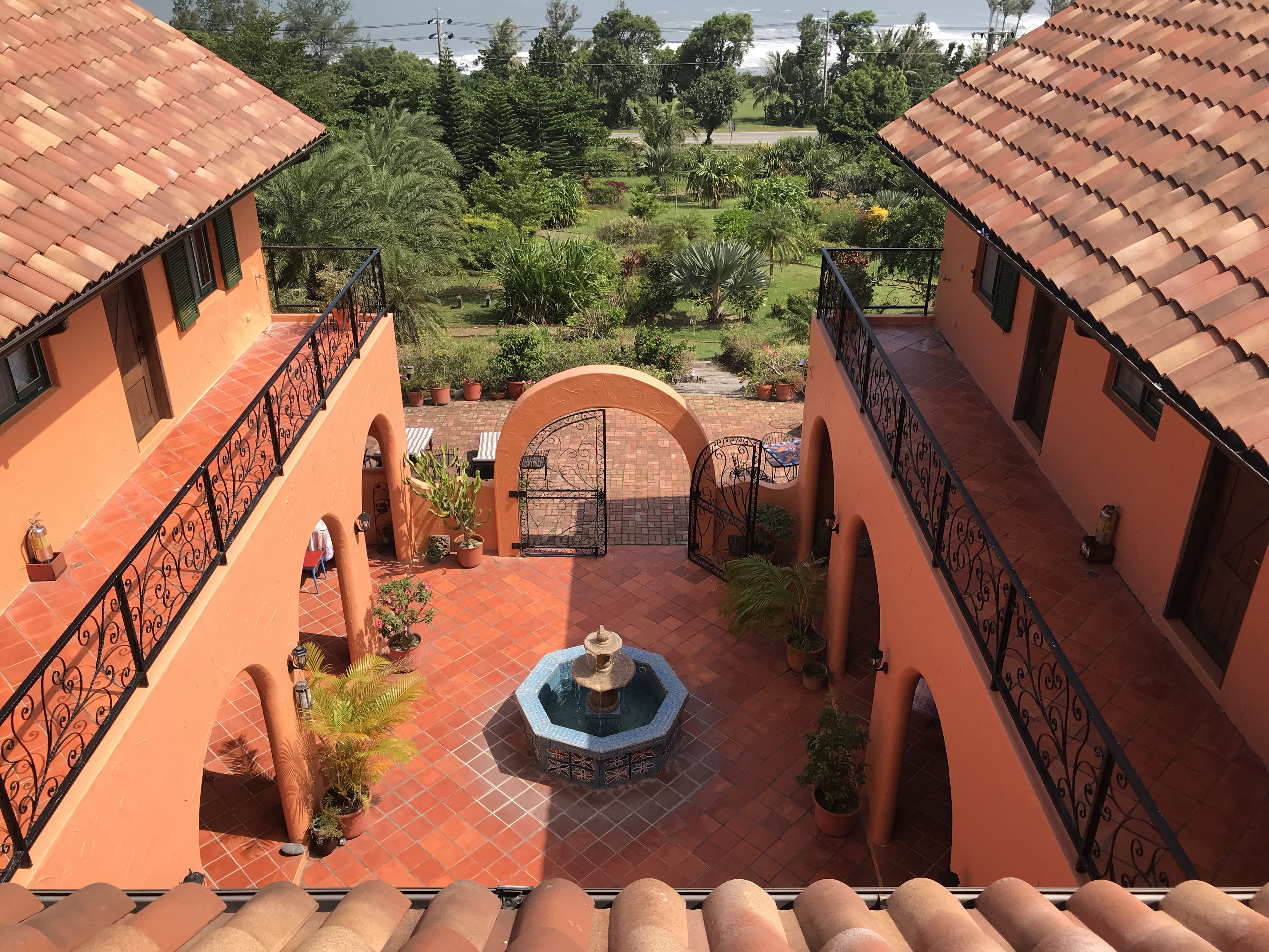 A courtyard with a fountain, surrounded by potted plants and a view of a lush garden.