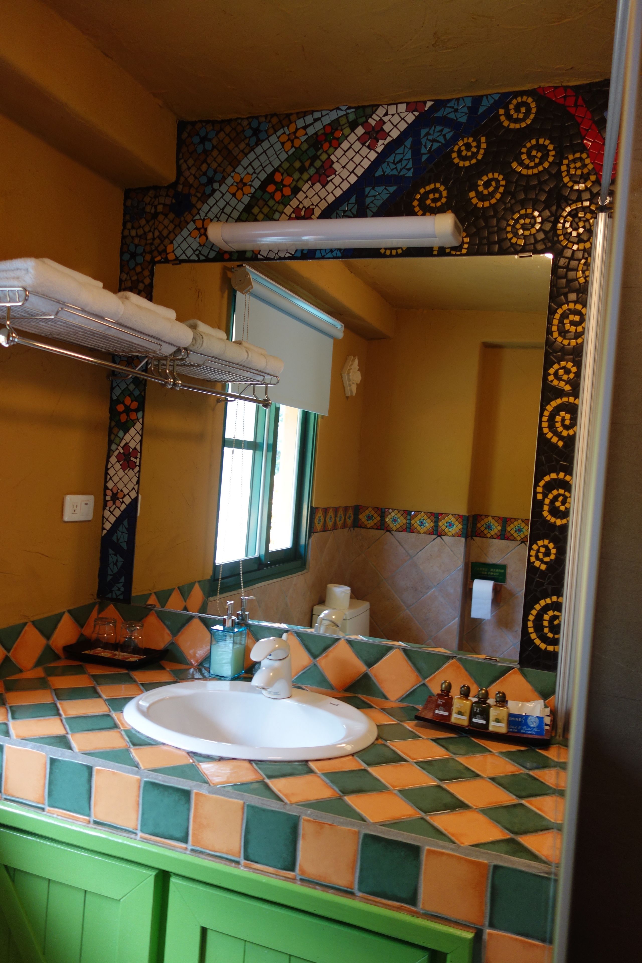 Un baño con lavamanos azulejado, un espejo y un perchero para toallas.