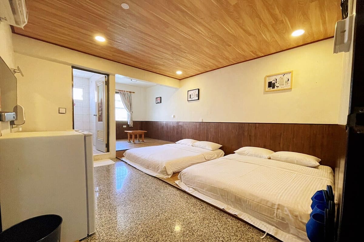 Habitación de hotel con dos camas, techo de madera, una mesita y una puerta que da al baño.