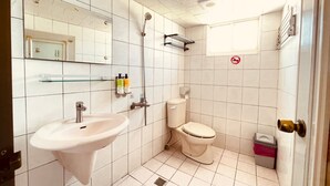 A small, clean bathroom with a sink, toilet, and shower. There is a mirror, a shelf with toiletries, and a trash bin. - Da Feng Homestay (Liuqiu)