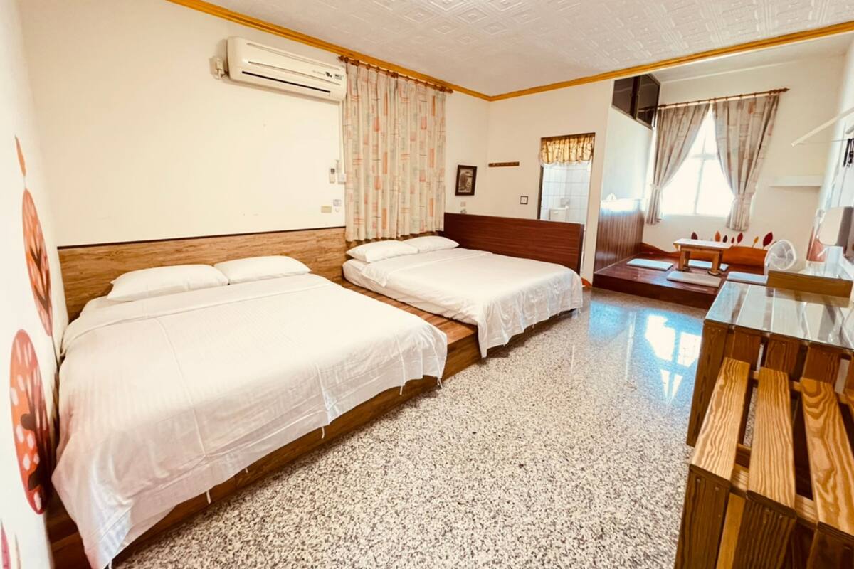 Habitación de hotel con dos camas individuales, cabecera de madera, un escritorio pequeño y un espejo.