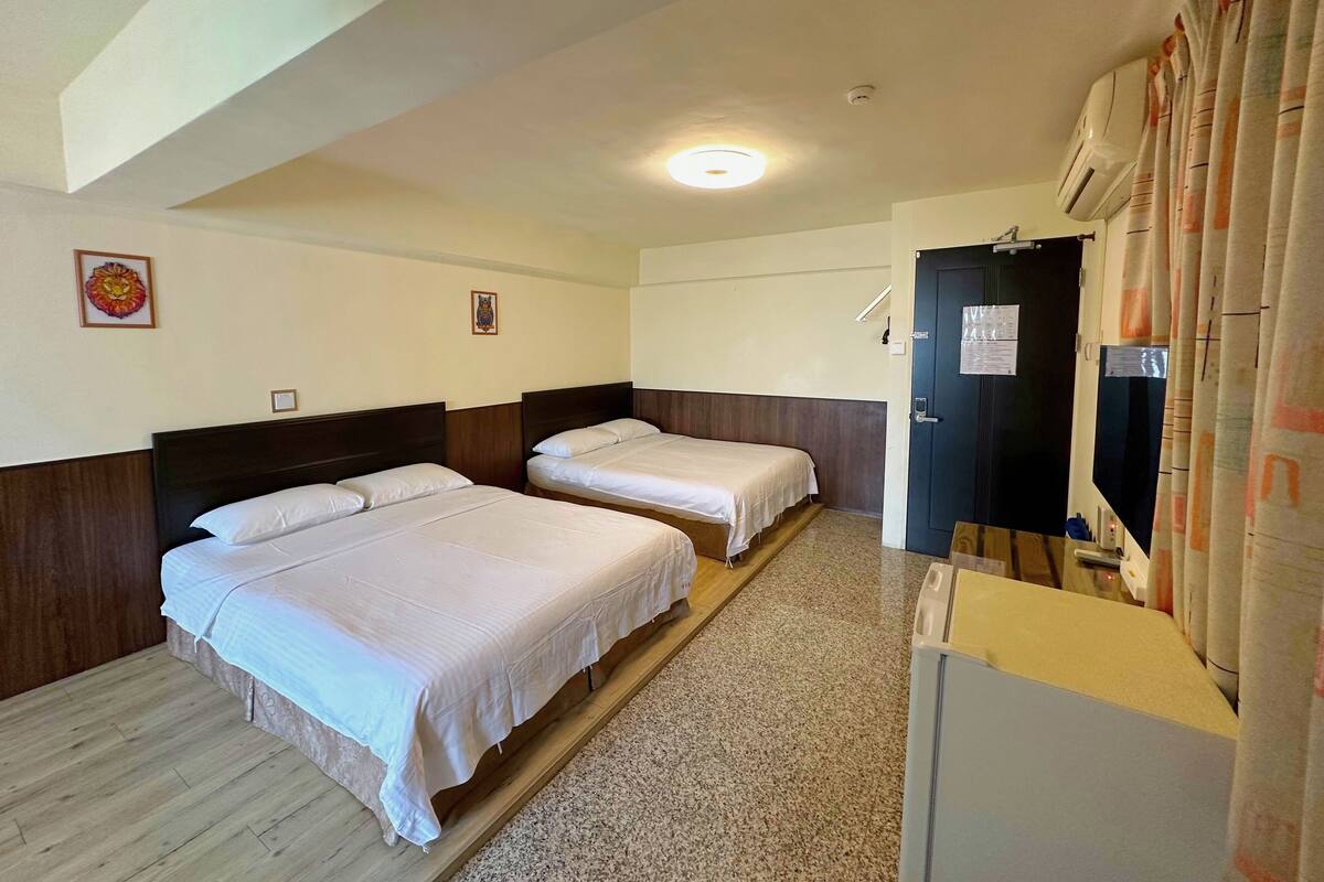 Habitación de hotel con dos camas, una puerta oscura, un escritorio pequeño y una luz en el techo.