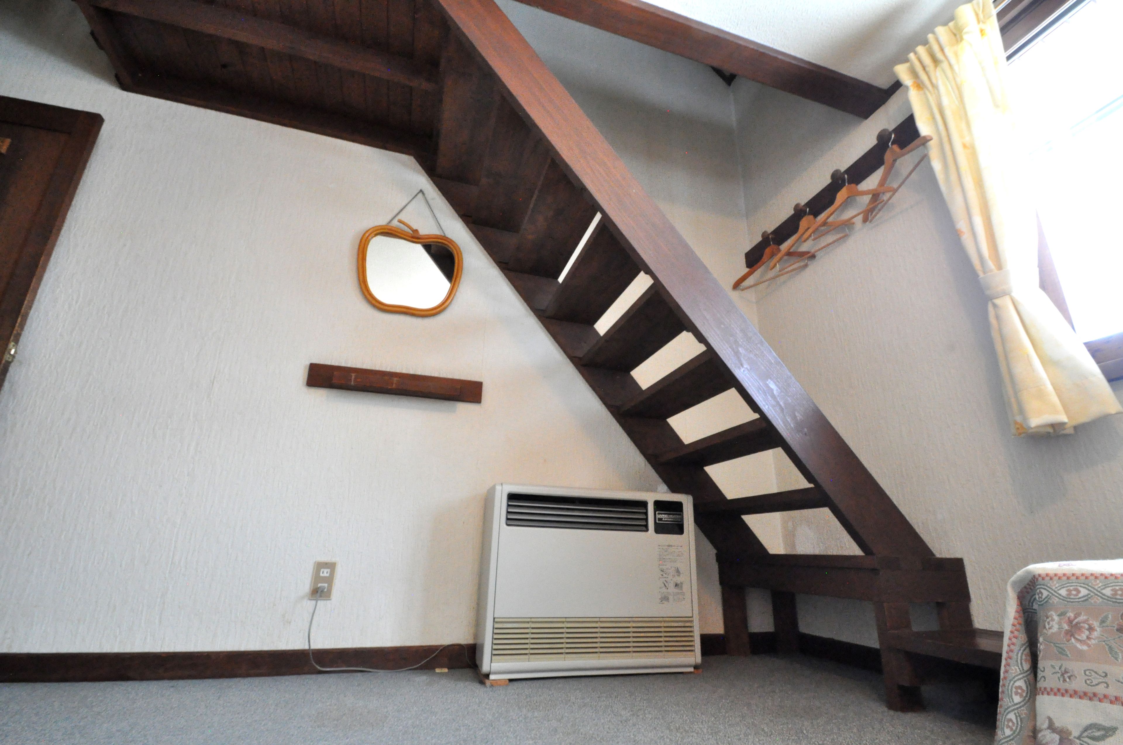 A room with a sloped ceiling, a wooden staircase, a white air conditioner, and a wall-mounted mirror.