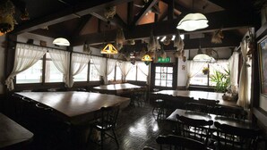 A restaurant with high ceilings, hanging light fixtures, and large windows with sheer curtains.