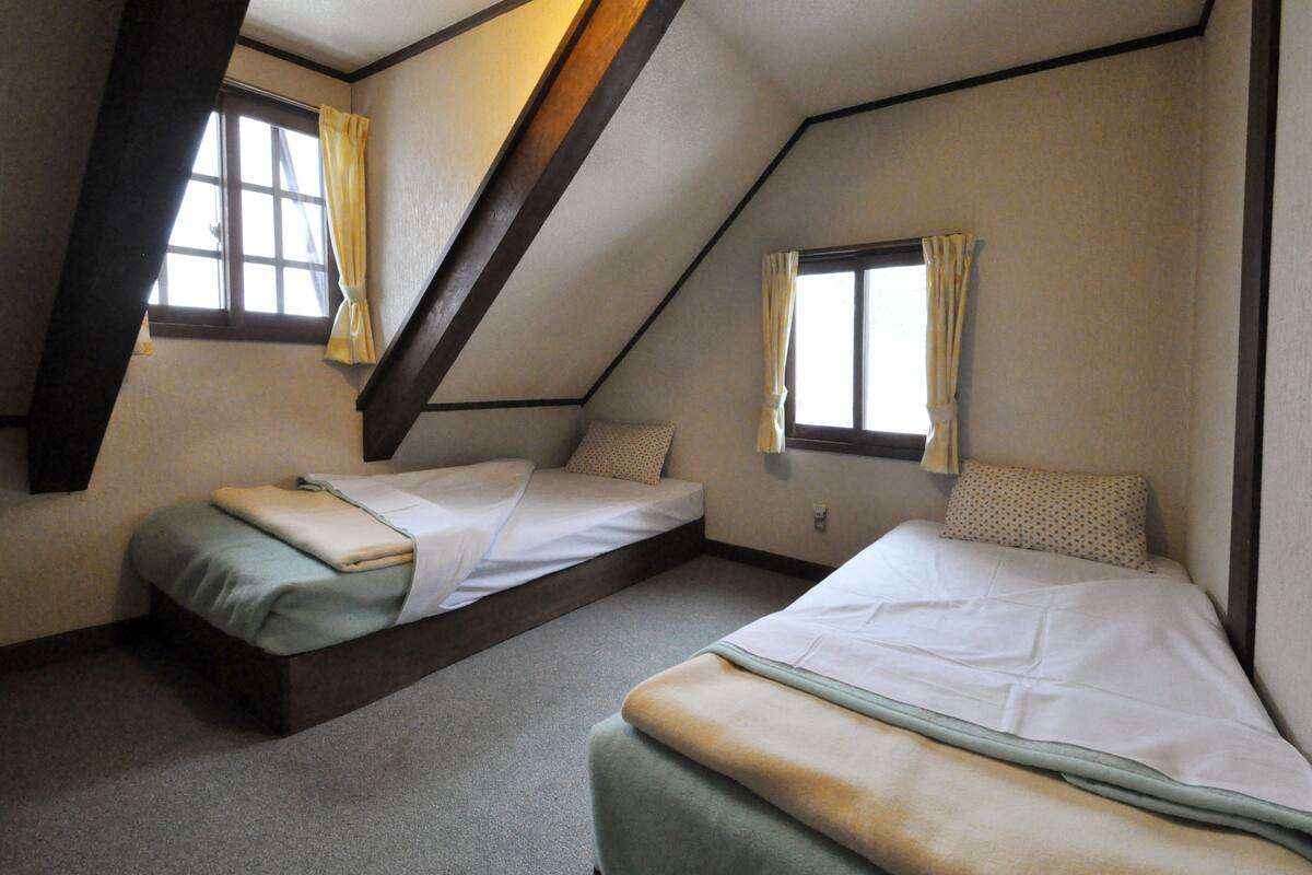 Ein Zimmer mit zwei Betten, einer geneigten Decke und Fenstern mit Vorhängen.