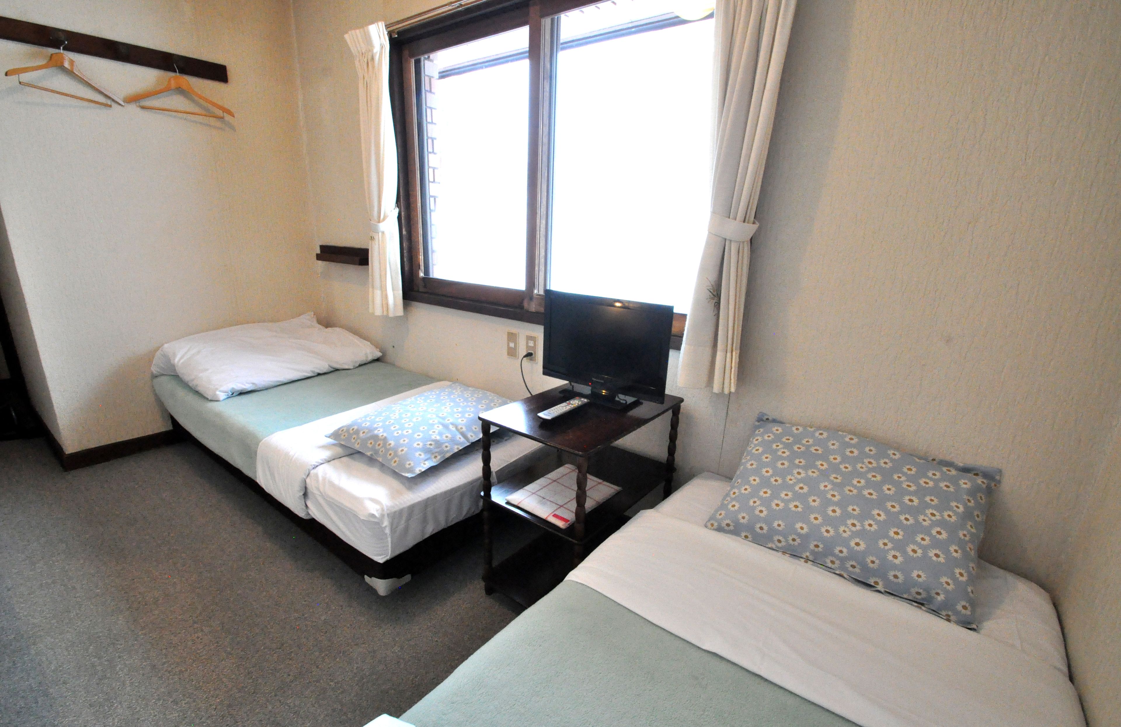 A small, compact room with two single beds, a TV on a wooden table, and a window with curtains.