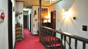 A hotel hallway with a red carpet, wooden railing, and a staircase.