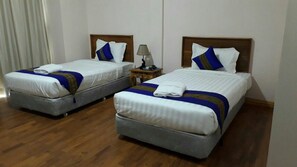Two single beds with wooden headboards, a small table with a lamp, and a wooden floor. - Famous Hotel Loikaw (Loikaw)