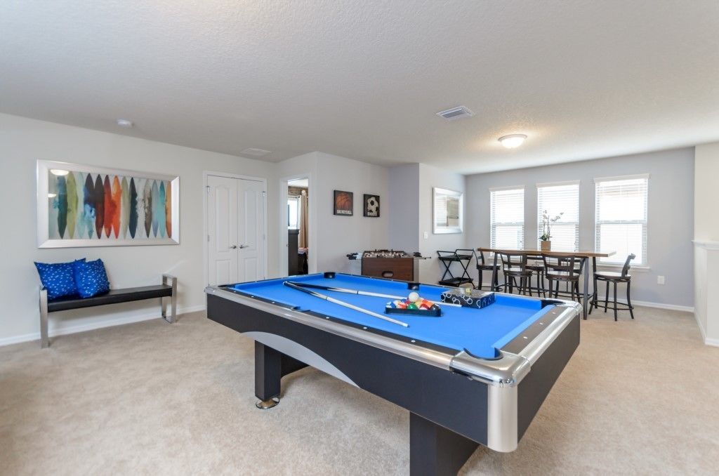 A pool table in a room with a bench, a table with chairs, and a painting on the wall.
