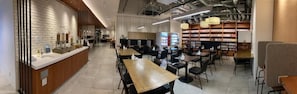 A modern cafe with a long counter, multiple tables, and a bookshelf.