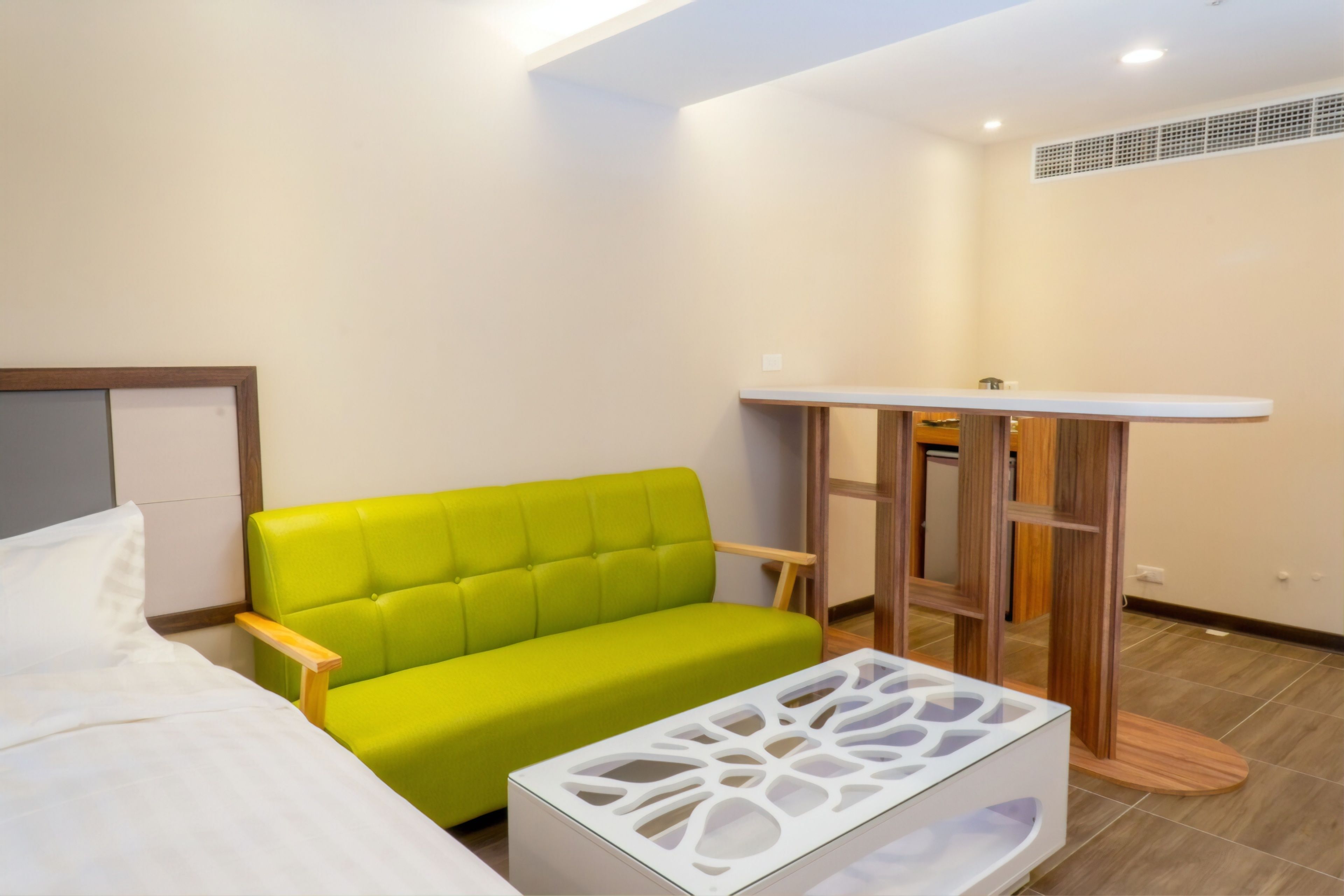 A modern hotel room with a green sofa, a white bed, and a unique white coffee table.