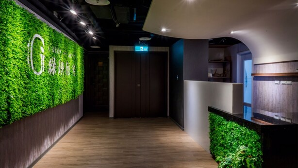A modern hotel corridor with a green wall, wooden flooring, and a reception area with a counter and shelves. - Greeninn Hotel (New Taipei City)
