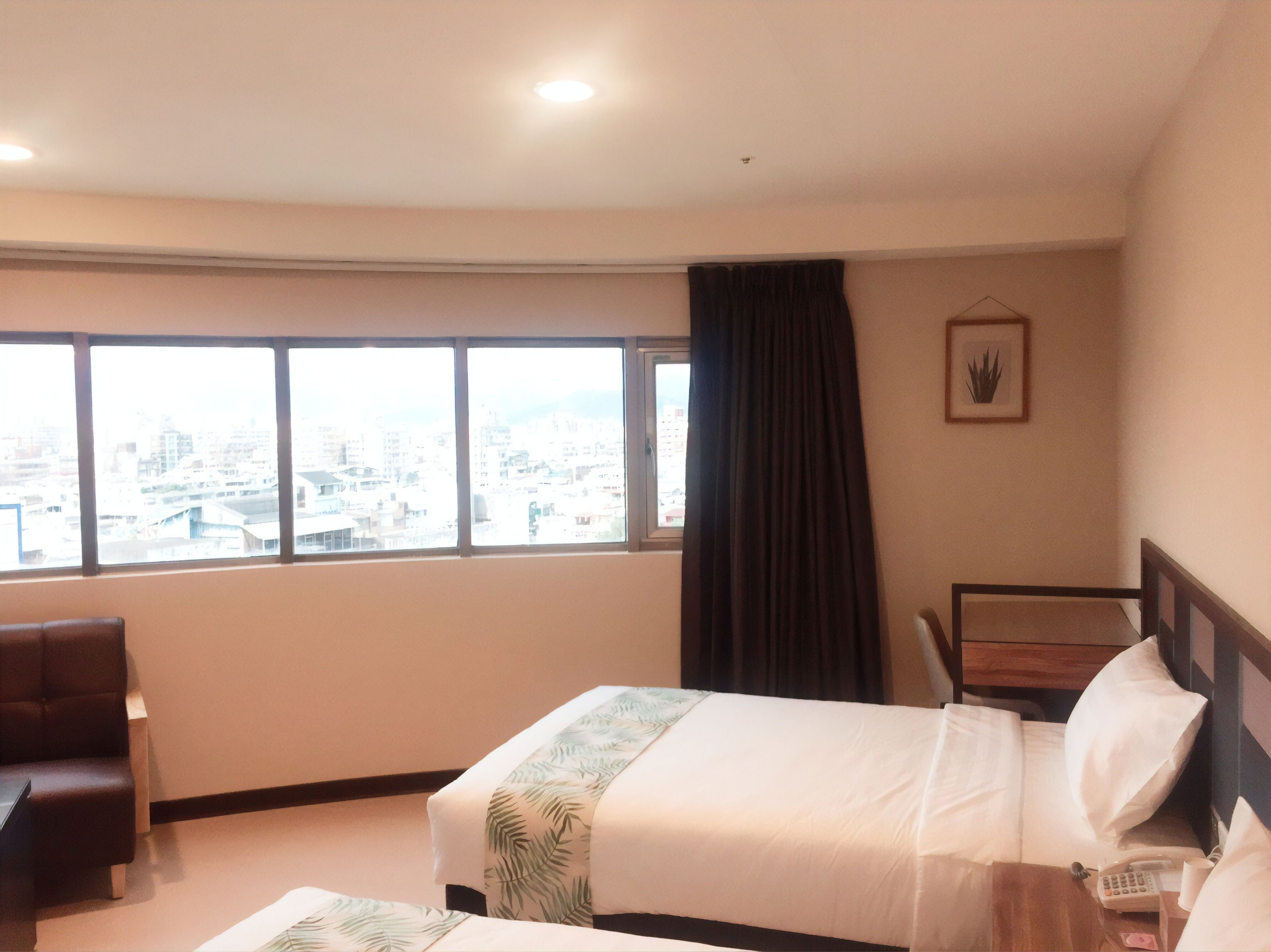 Een hotelkamer met een bed, een stoel, een bureau en een groot raam met uitzicht op de stad.