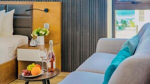 Une chambre d’hôtel moderne avec un lit, une petite table sur laquelle se trouve une assiette de fruits, une bouteille de vin et un vase de fleurs.