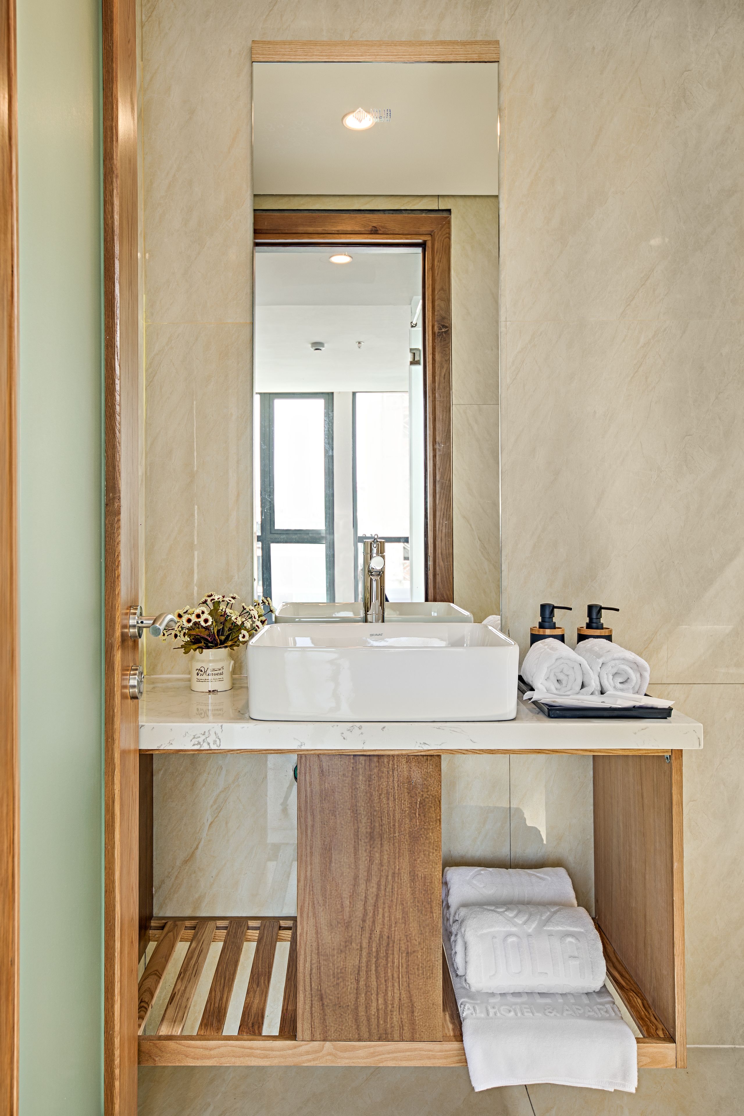 A bathroom with a white sink, wooden vanity, and a mirror. There are towels and toiletries on the counter.