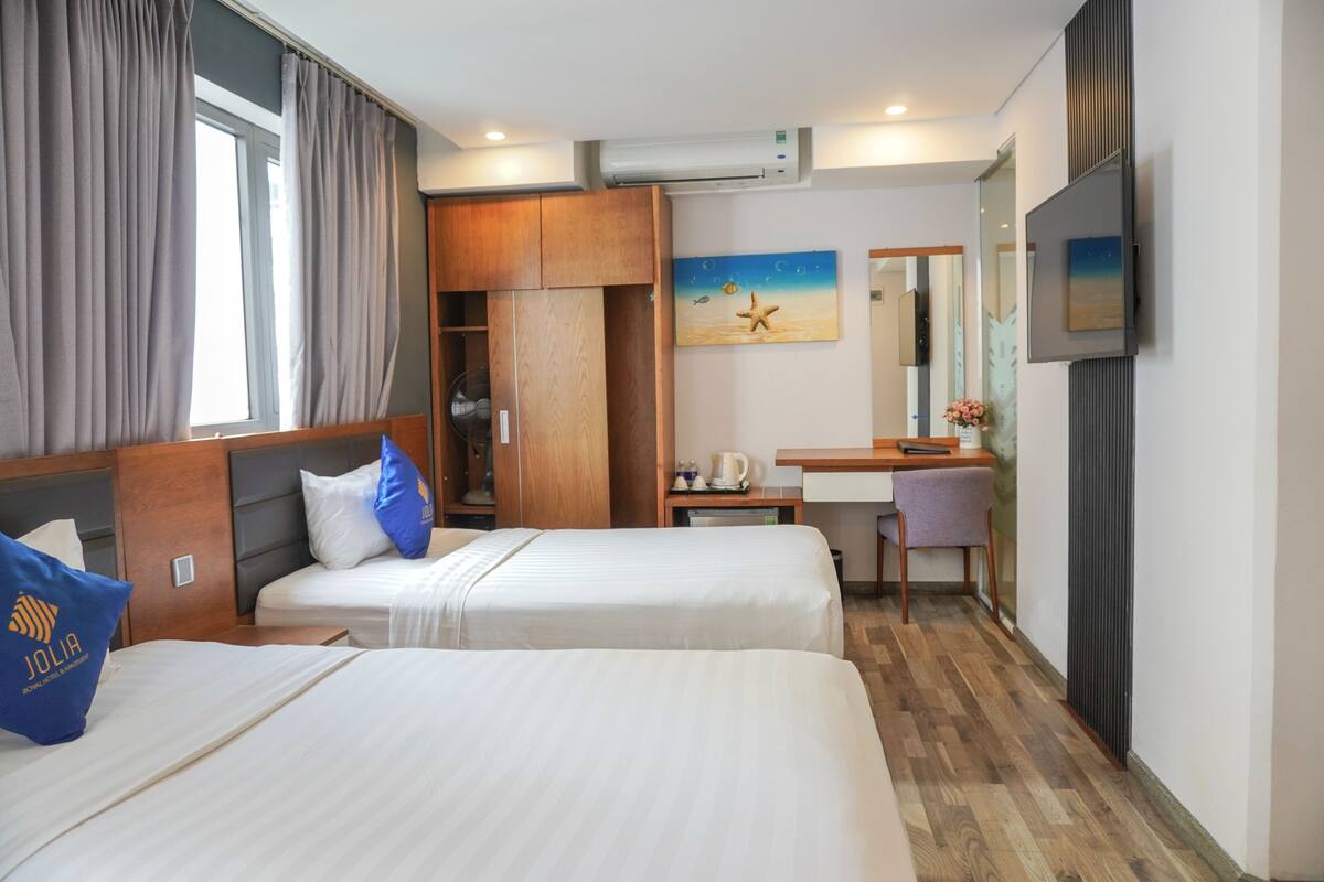 Una habitación de hotel con dos camas, un escritorio, una silla, un televisor y un cuadro en la pared.