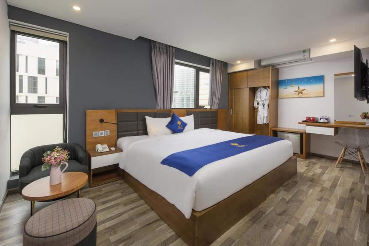 Habitación de hotel con una cama grande, un escritorio, una silla, una mesita con un florero y un televisor.