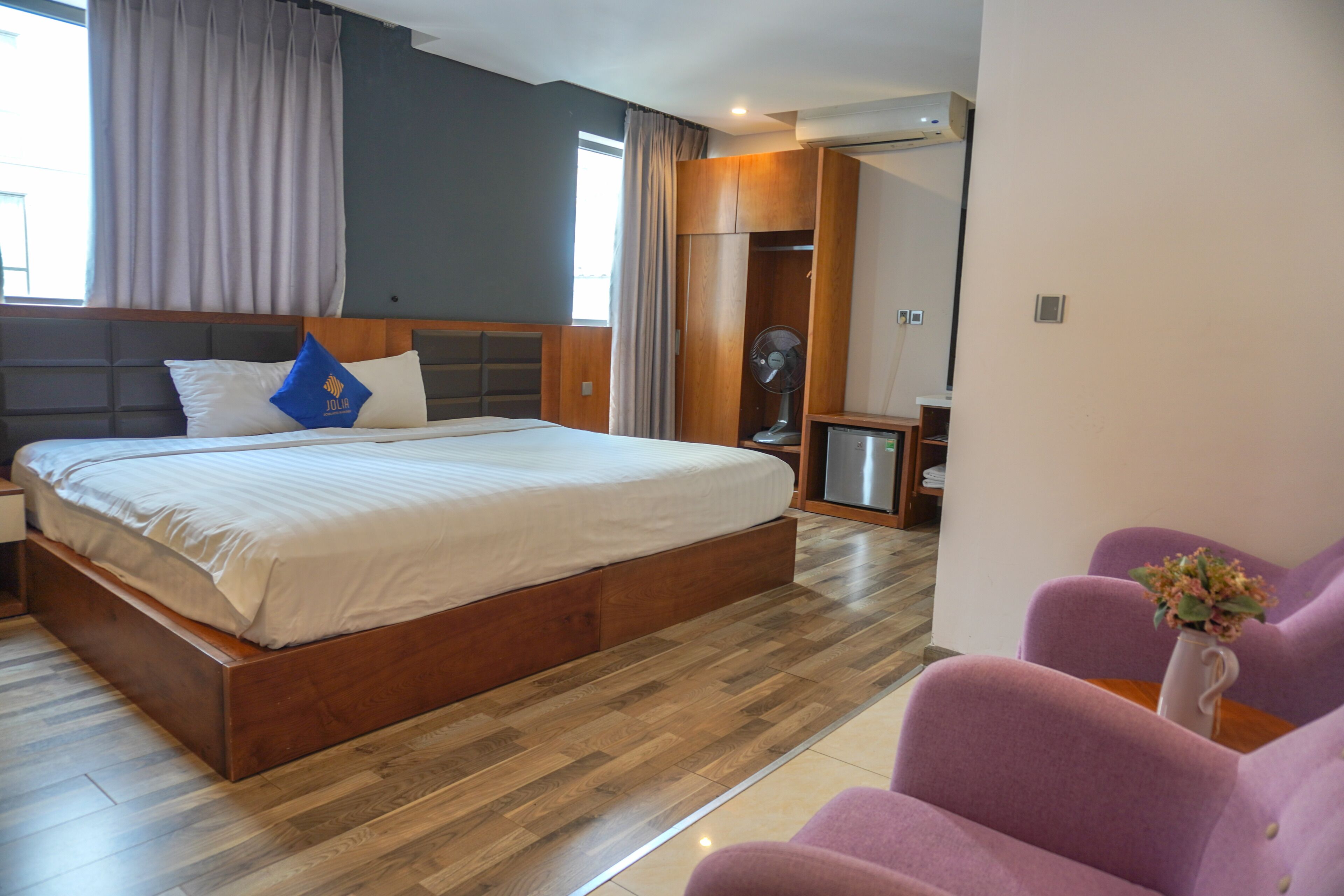 A modern hotel room with a large bed, wooden headboard, and a built-in wardrobe.