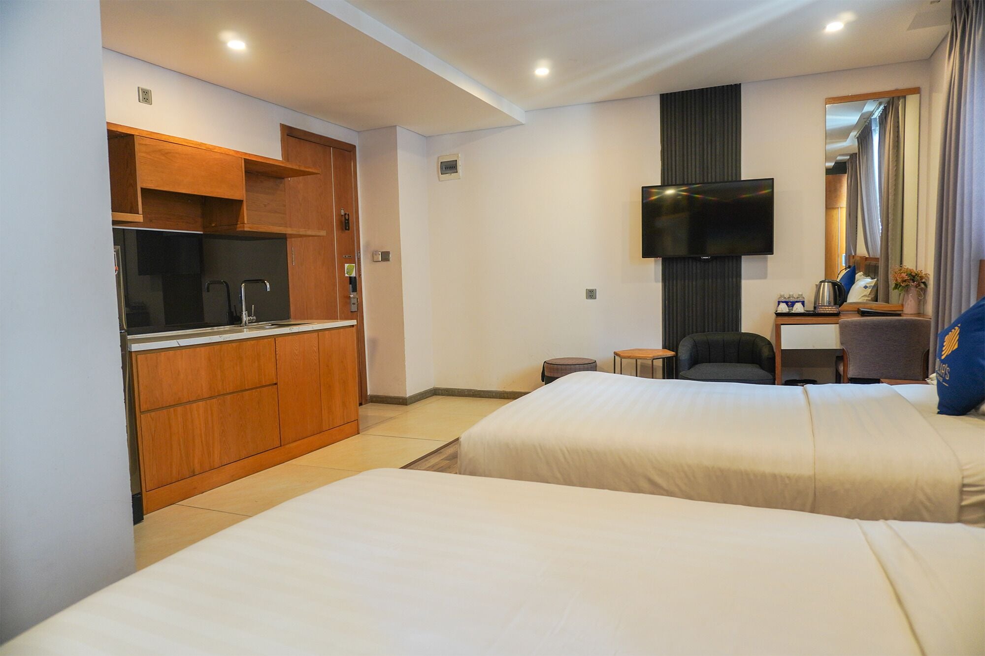 Une chambre d’hôtel avec deux lits, une kitchenette, un téléviseur à écran plat et une petite table avec une chaise.