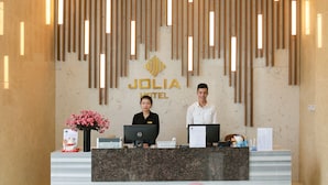 Mostrador de recepción en el HOTEL JOLIA con un diseño moderno, que presenta una pared de mármol y listones verticales de madera.