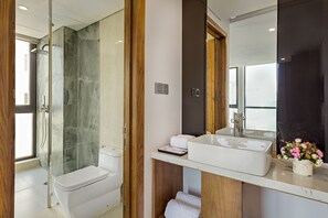 A modern bathroom with a glass-enclosed shower, a white toilet, a sink with a mirror, and a window providing natural light. - Jolia Hotel Danang Beach (Da Nang)