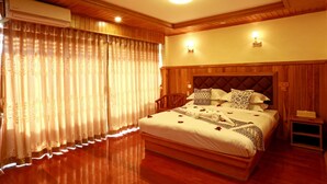 Habitación de hotel con cama de madera, cabecera, mesita de noche y ventana con cortinas.