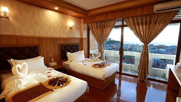 Habitación de hotel con dos camas, paneles de madera, vistas a la ciudad y un balcón.