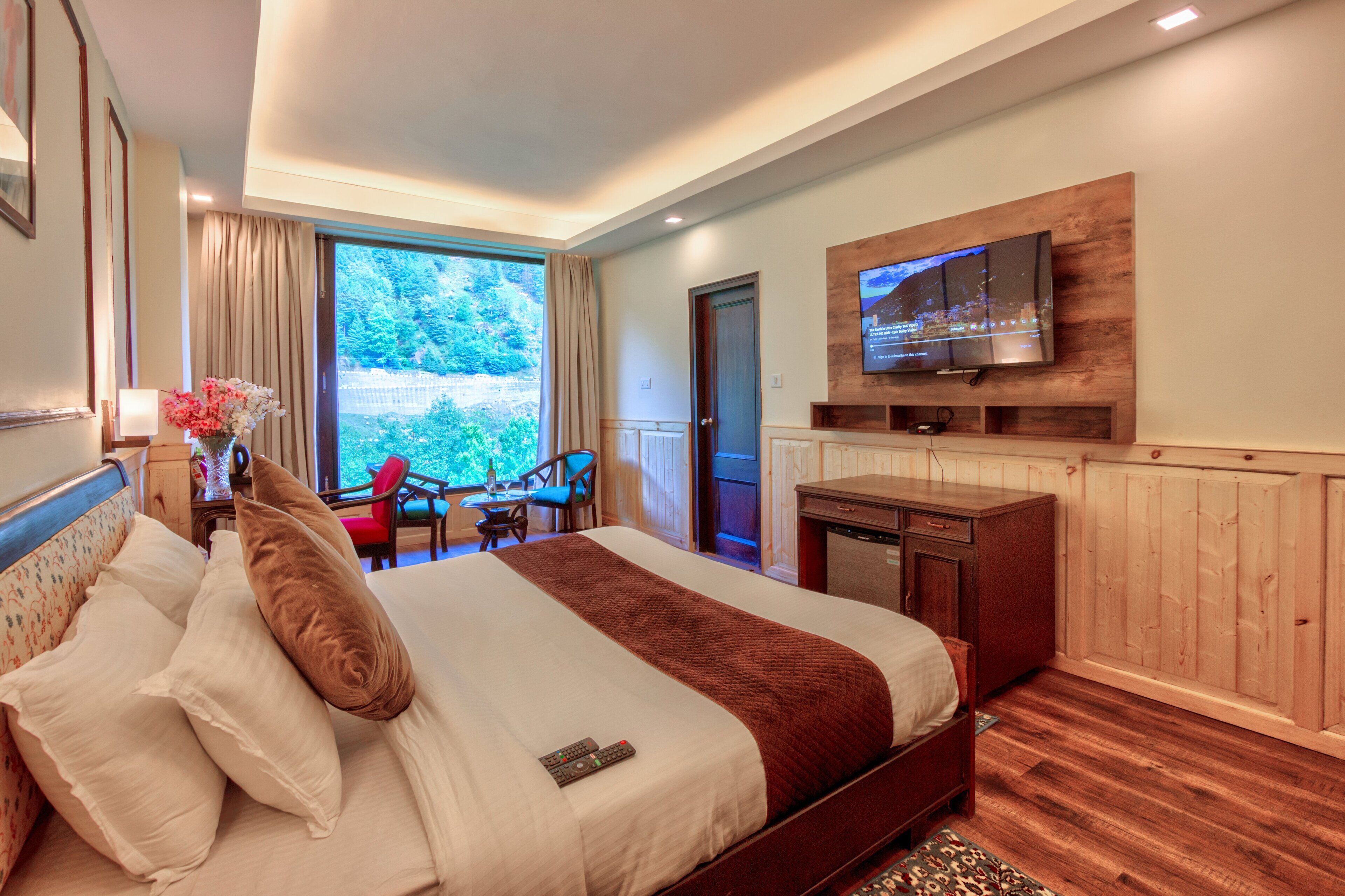 Habitación de hotel con una cama grande, un televisor montado en la pared, un escritorio con una silla y vistas a zonas verdes.