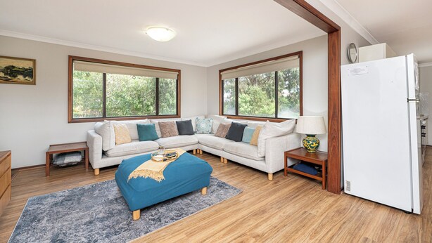 A living room with a sectional sofa, a blue ottoman, a wooden floor, and a white refrigerator. - Relax Moore - Walking distance to Beach. (Guilderton)
