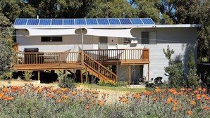 Une maison mobile dotée de panneaux solaires, d’une terrasse en bois et d’un jardin agrémenté de fleurs oranges.
