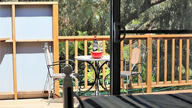 Une terrasse en bois avec une table et des chaises, un petit bol rouge et une bouteille de vin.