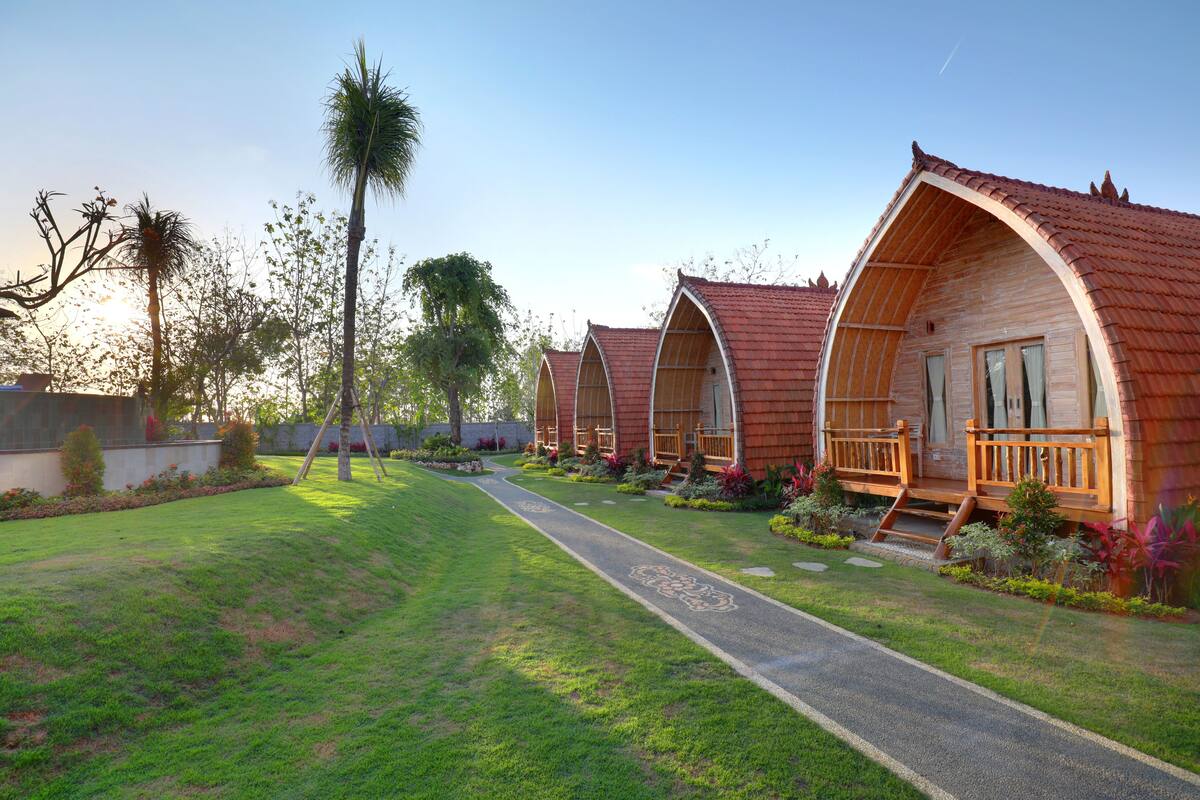 A row of wooden cabins with pitched roofs, a paved pathway, and landscaped gardens.