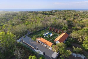 Vista aérea de un complejo turístico con varias cabañas, una piscina y vistas al océano.
