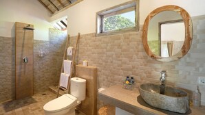 Un baño con ducha de baldosas de piedra, una escalera de madera, inodoro, lavabo de piedra y un espejo con marco de madera.