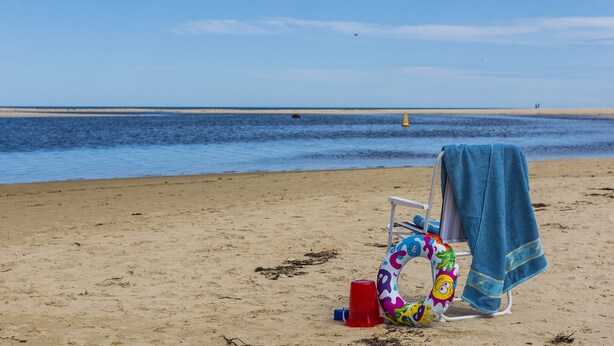 A beach with a chair covered by a blue towel, a colorful inflatable ring, and a red bucket. - Blueshack - Walking distance to foreshore (Guilderton)